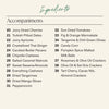 A printed ingredients list titled 'Ingredients' with the subheading 'Accompaniments' on a light beige background. The list includes items such as Juicy Dried Cherries, Turkish Pitted Dates, Fig & Orange Marmalade, Sun Dried Tomatoes, and Rosemary & Olive Oil Crackers, numbered 20 through 39.