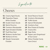 A clean ingredients list titled 'Cheeses' for the Boarderie Happy Holidays All Cheese Large Board on a light beige background, with 20 cheese varieties listed in two columns and a green 'MORE →' link at the bottom right.