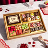 Valentines Day dessert board with "I love you" message, decorated truffles, macarons, candies, and fruit gummies in gold compartments for gifting.