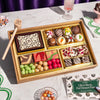 Medium chocolate dessert board featuring colorful macarons, decorated truffles, chocolate shards, gourmet candies, and fruit gummies arranged in gold compartments with a wooden smashing mallet.
