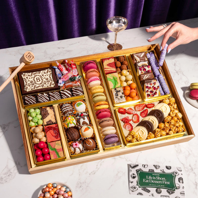 Gourmet dessert gift board featuring over 47 artisan chocolates, brownies, macarons, cakes, truffles, caramels & more on a reusable acacia wood board. Smash the chocolate box for a surprise.
