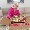 woman in a pink blazer holding a festive charcuterie board decorated with heart & 'XO' cheese shapes