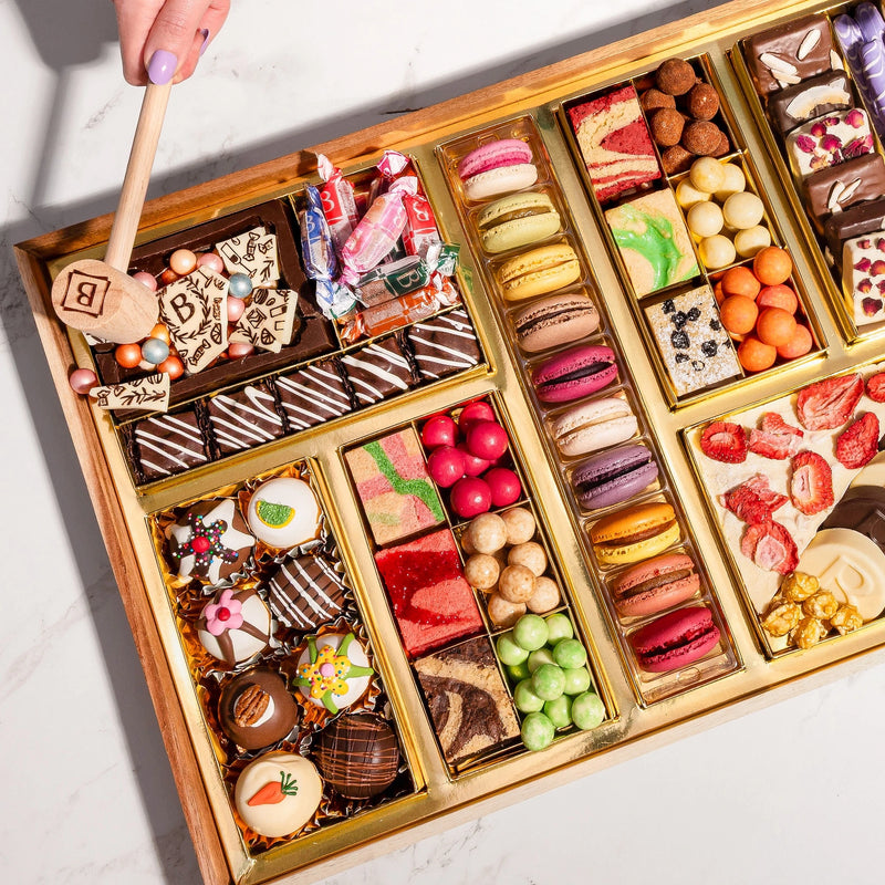 Gourmet dessert gift board featuring over 47 artisan chocolates, brownies, macarons, cakes, truffles, caramels & more on a reusable acacia wood board. Smash the chocolate box for a surprise.