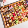 Valentines Day dessert board with wooden mallet, featuring macarons, decorated truffles, candies, strawberries, and gourmet treats in gold compartments for smashing.