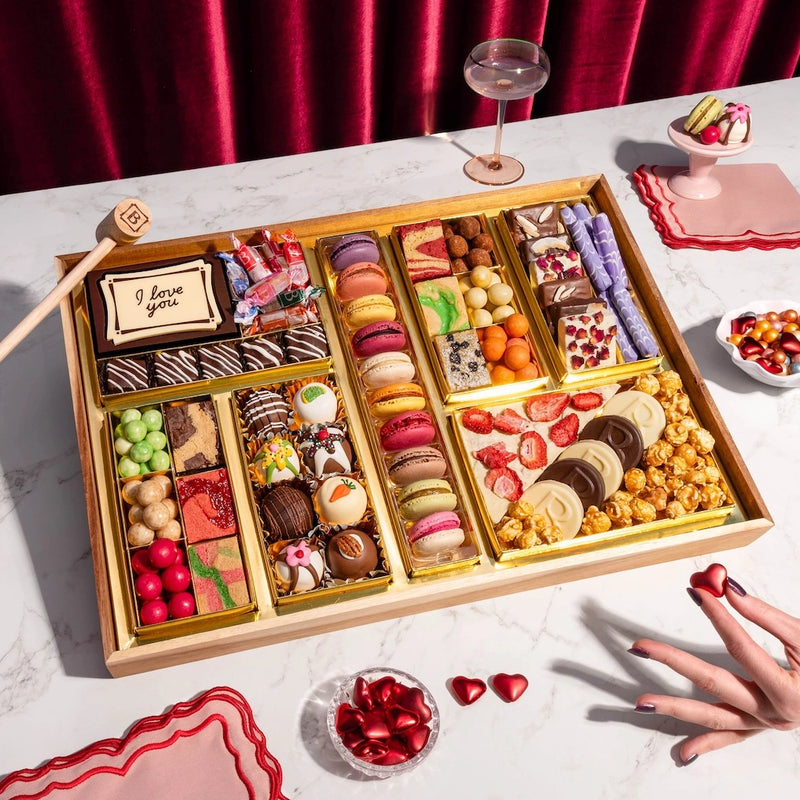 Large dessert board with "I love you" message, macarons, decorated truffles, candies, strawberries, and popcorn in gold compartments for Valentine's Day.