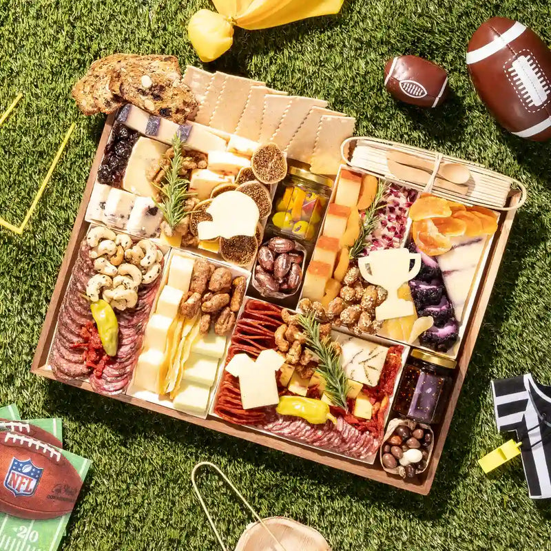 Football charcuterie board with gourmet cheeses, meats, nuts, and cheese cutouts shaped like a helmet, jersey, and trophy 