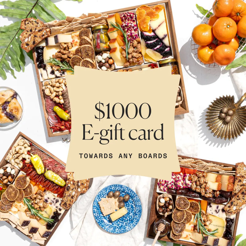 Assorted gourmet charcuterie boards with cheeses and snacks, promoting a $1000 e-gift card towards any board selection.