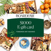 Boarderie $1000 e-gift card displayed on green background surrounded by gourmet charcuterie boards filled with cheese, cured meats, nuts, and fresh citrus.