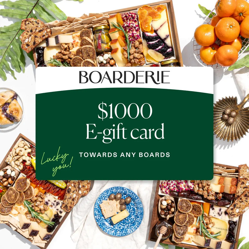 Boarderie $1000 e-gift card displayed on green background surrounded by gourmet charcuterie boards filled with cheese, cured meats, nuts, and fresh citrus.