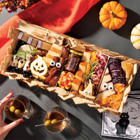 medium size halloween charcuterie board featuring festive cheese shapes, candy corn, meats, and nuts, with pumpkins and cocktails nearby