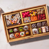 A wooden gift box filled with assorted Halloween-themed chocolates, candies, and treats, photographed from above on a light marble surface.