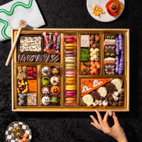 Overhead view of the Boarderie Large Halloween Dessert Board featuring 47-plus gourmet Halloween treats, artisan macarons, spooky truffles, brownies, and a chocolate smash box on a black background.