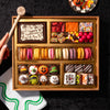 Overhead view of the Boarderie Medium Halloween Dessert Board featuring a hand holding a wooden hammer next to a Happy Halloween chocolate smash box, surrounded by gourmet confections, French macarons, and hand-decorated Halloween truffles.