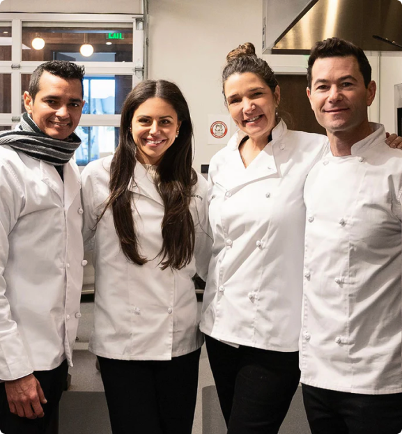 Group of four Boarderie chefs in white uniforms smiling together in a professional kitchen.