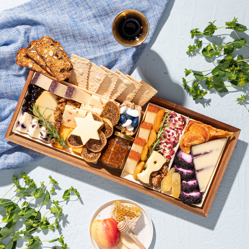 Jewish High Holiday charcuterie board gift with assorted cheeses, crackers, figs, dried fruits, honeycomb, & star-shaped cheese decorations for a festive touch