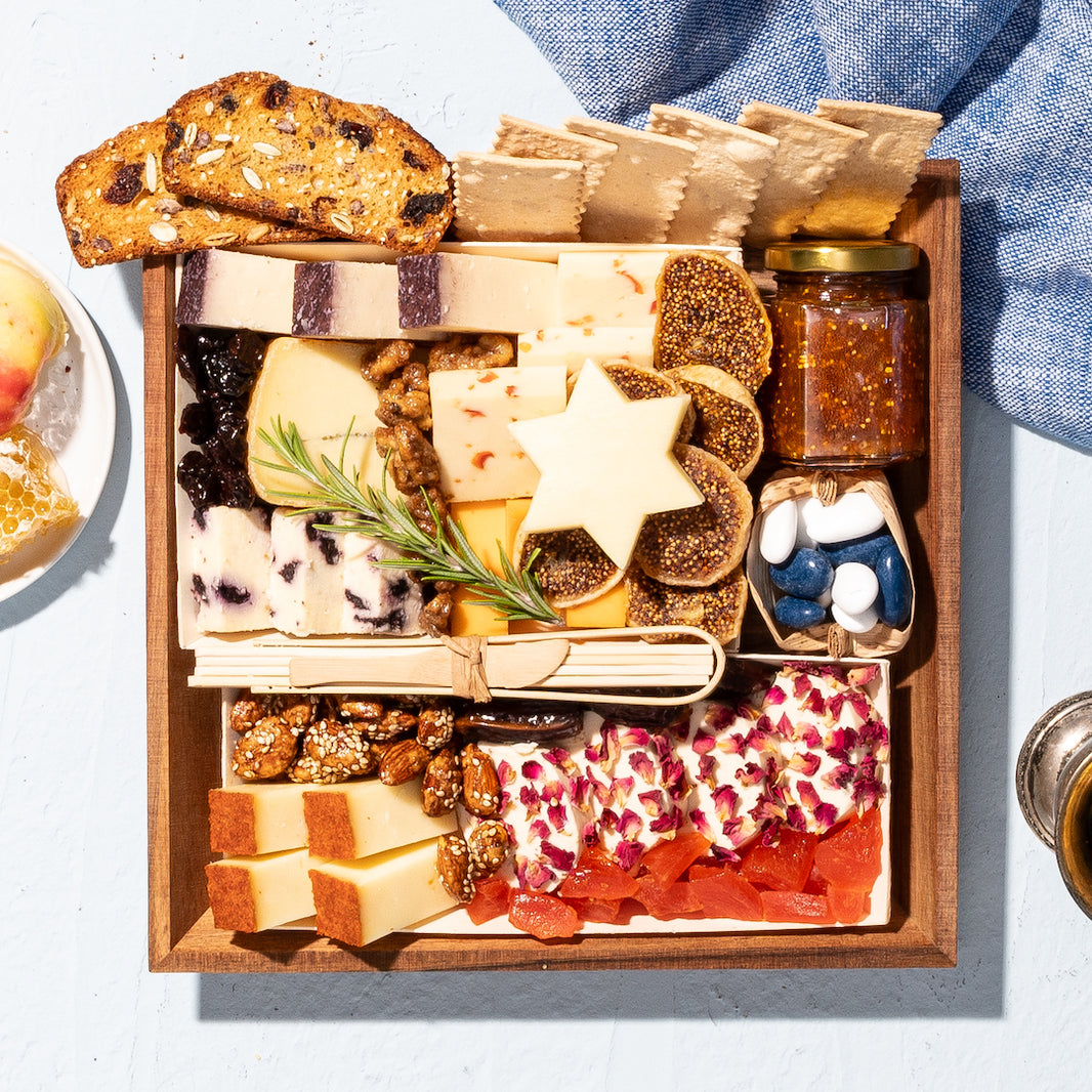 Jewish High Holiday charcuterie board featuring cheeses, dried fruits, nuts, fig jam, crackers, & a Star of David cheese cutout