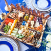 Large Jewish holiday cheese board with matzo, assorted cheeses, cured meats, nuts, olives, fresh fruit, and decorative elements arranged in compartments for Passover celebration.