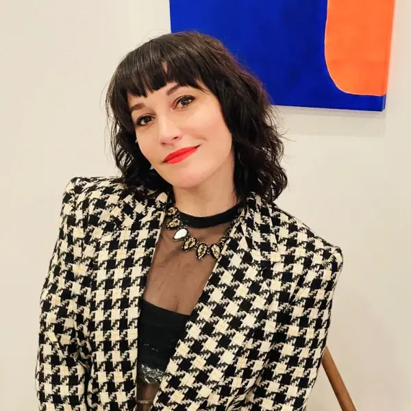 Leia Perkins with short dark hair and red lipstick wearing a black and white houndstooth jacket and statement necklace.