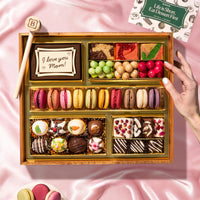 Assorted chocolate box with a hand reaching towards it on a pink fabric background