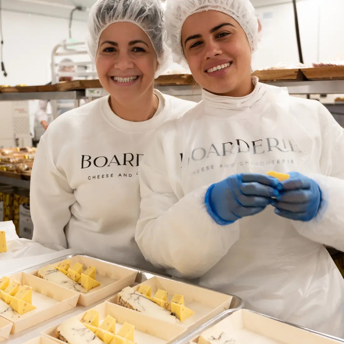 Boarderie cheesemakers in protective gear preparing cheese trays with neatly arranged slices in a processing facility.