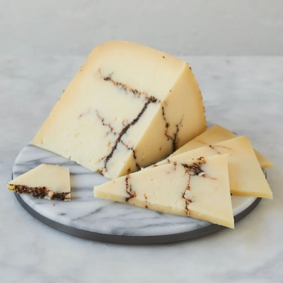 Wedge of truffle-infused cheese with visible marbling, sliced into triangular pieces on a marble serving board.