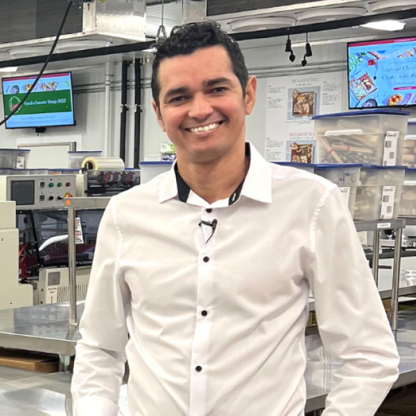 Angel Jerez in a white dress shirt smiling in a modern industrial kitchen or food production facility.