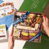 Artisan cheese & charcuterie boards with gourmet meats, cheeses, nuts, dried fruits, olives, and rosemary garnish in gift packaging.