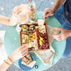 Two people enjoying a small charcuterie board with meats, cheeses, and nuts, paired with drinks on a round table.