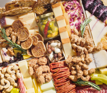 Charcuterie board close-up with assorted cheeses, figs, nuts, meats, and pickled vegetables arranged neatly.