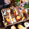 Large Thanksgiving charcuterie board with maple leaf-shaped cheese cutouts, assorted cheeses, cured meats, nuts, pickled vegetables, whole grain bread, and autumn harvest decorations.