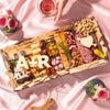 Luxury Valentine’s Day charcuterie board gift by Boarderie featuring artisan cheeses, cured meats, dried fruits, nuts, crackers, gourmet spreads, and customized initials in cheese. Board is on a pink romantic backdrop, styled for nationwide overnight gifting. 