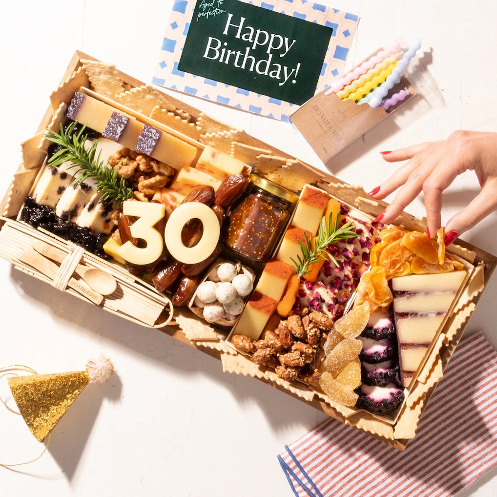 Birthday cheese board featuring "30" cheese numbers, a variety of cheeses, dried fruits, nuts, and festive birthday decorations.