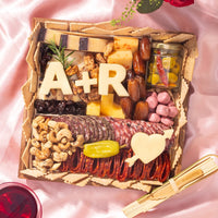 Engagement charcuterie board with meats, cheeses, nuts, and custom cheese cutouts of initials and a heart with arrow.