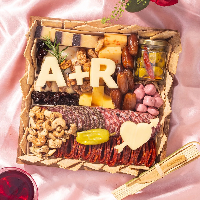 Engagement charcuterie board with meats, cheeses, nuts, and custom cheese cutouts of initials and a heart with arrow.