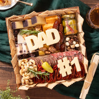 Charcuterie board for Father’s Day featuring meats, cheeses, nuts, pickles, and cheese cutouts spelling “DAD” and “#1”.