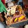 Halloween-themed charcuterie board with jack-o'-lantern cheese cutout, googly-eyed candy treats, cured meats, nuts, olives, and white decorative pumpkin.
