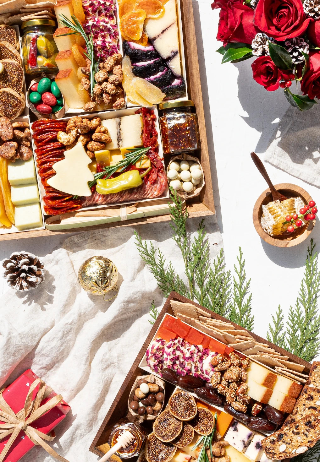 Charcuterie board festive gift with assorted cheeses, meats, nuts, and holiday-themed decorations, surrounded by greenery and wrapped presents.