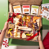 Holiday-themed cheese and charcuterie board with festive cheese shapes, nuts, dried fruits, and crackers, tied with a red ribbon and boxed with artisan crisps.