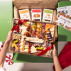 Holiday-themed cheese and charcuterie board with festive cheese shapes, nuts, dried fruits, and crackers, tied with a red ribbon and boxed with artisan crisps.