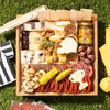 Football themed charcuterie board with cheeses, meats, crackers, nuts, and football-inspired cheese cutouts on a grass picnic setting.