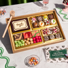 Dessert treat box with a "Thank you" chocolate plaque, decorated chocolate truffles, brownies, rose petal bark, and colorful candy balls in a gold-lined wooden tray beside a Boarderie gift card