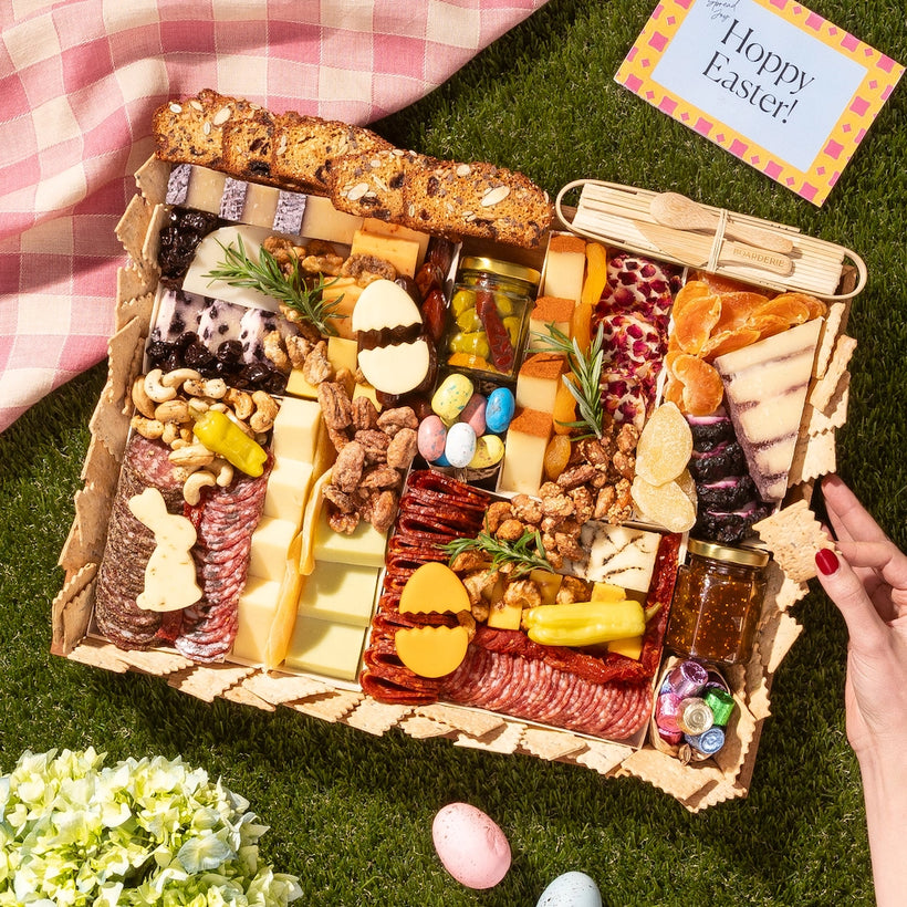 Easter charcuterie board filled with cheeses, meats, crackers, nuts, dried fruits, and festive egg-shaped treats on a picnic setting.