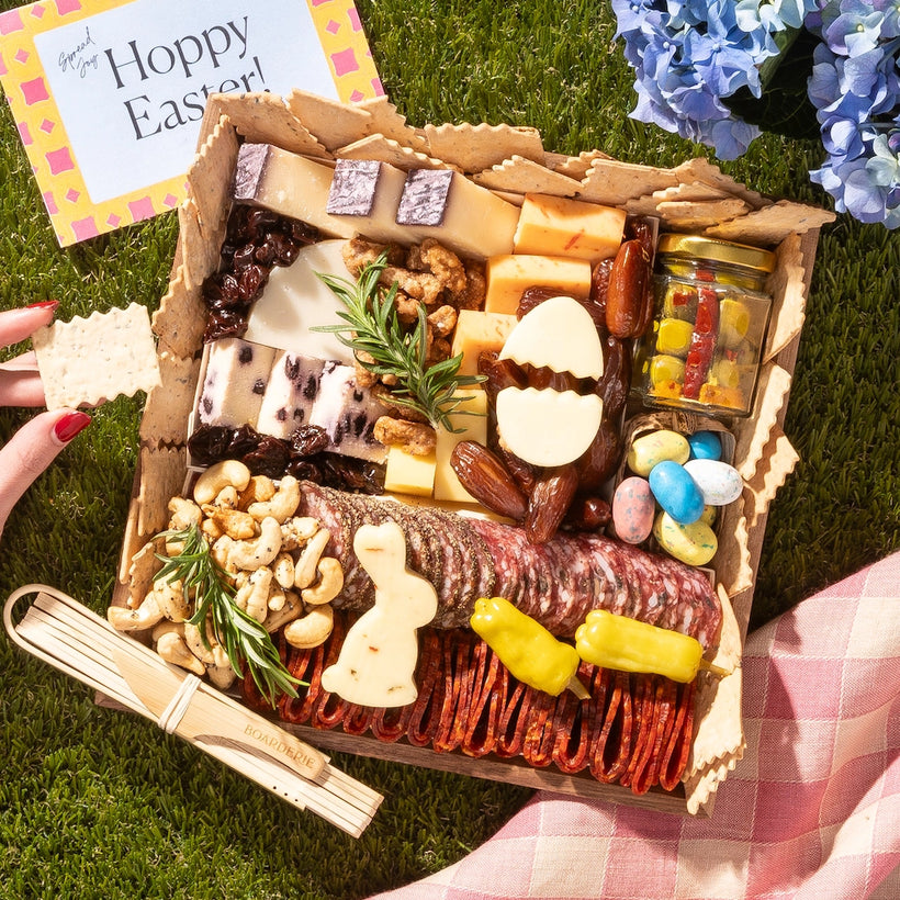 Easter charcuterie board featuring cheeses, meats, crackers, nuts, and festive egg and bunny-shaped treats on a picnic setup.