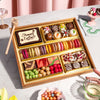 Medium Easter dessert board loaded with two rows of colorful macarons, decorated chocolate truffles, a "Happy Easter" chocolate plaque, brownies, rose petal bark, and candy balls in a gold-lined wooden tray