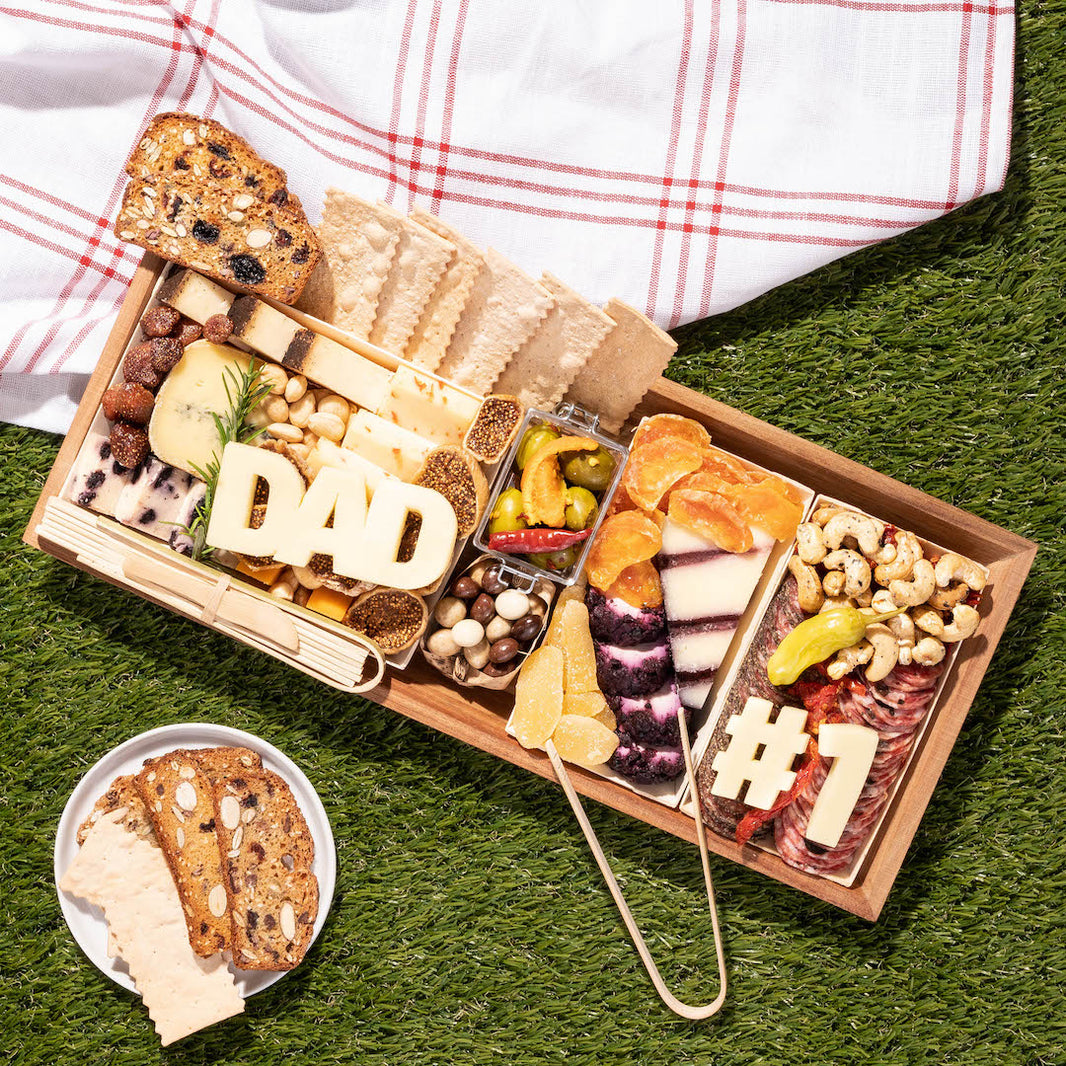 Father's Day charcuterie board on grass with cheese, meats, dried fruits, and crackers arranged with "DAD" and "#1" cheese cutouts.