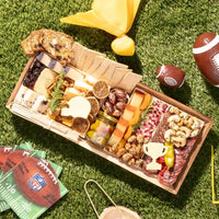 Football charcuterie board featuring cheeses, meats, crackers, nuts, and football-themed cheese cutouts on a picnic setting.