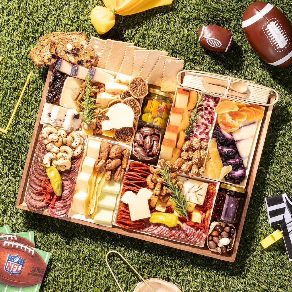 Football-themed charcuterie board with meats, cheeses, and snacks arranged on grass with football decorations and napkins.