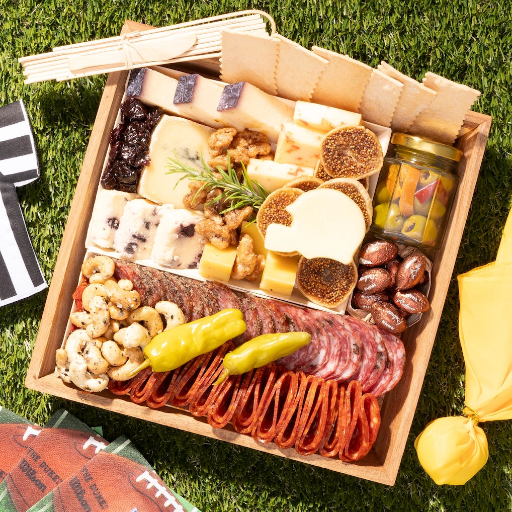 Football-themed charcuterie board with assorted cheeses, meats, nuts, and pickles, arranged for a game day snack spread.