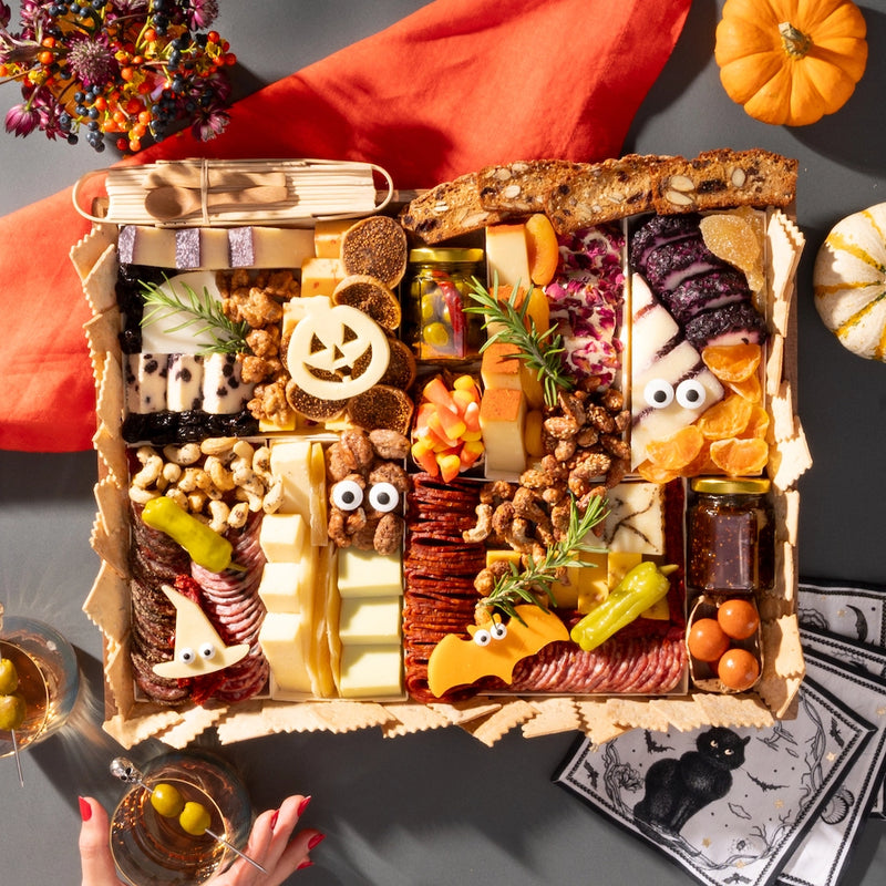 Halloween-themed charcuterie board featuring festive cheeses shaped like a pumpkin and bat, surrounded by assorted snacks and decorations.