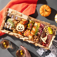 medium halloween charcuterie board featuring festive cheese shapes, candy corn, meats, and nuts, with pumpkins and cocktails nearby.